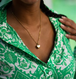 Woman wearing a small gold heart cremation necklace holding pet ashes